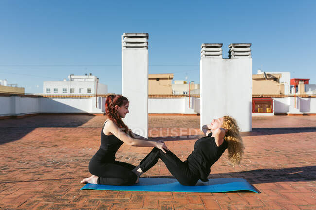 Женщины практикуют партнерскую йогу на крыше — стоковое фото