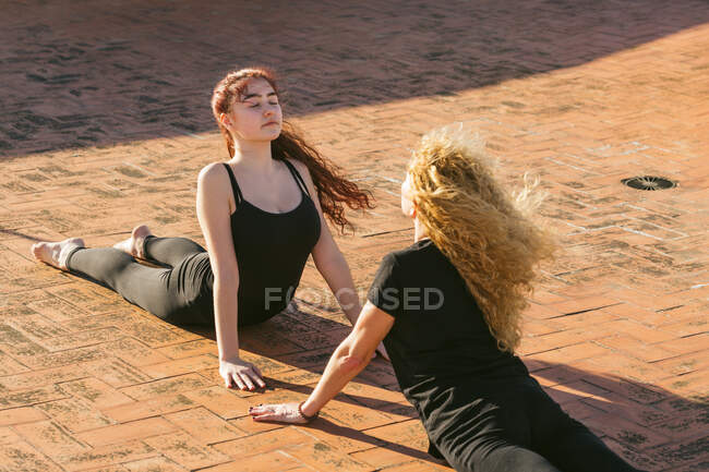 High angle of young and middle aged women in black sportswear doing Cobra pose while practicing yoga together on sunny terrace — Stock Photo