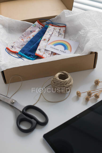 Máscaras hechas a mano con tarjeta de agradecimiento en caja, hilo y tijeras en la mesa - foto de stock