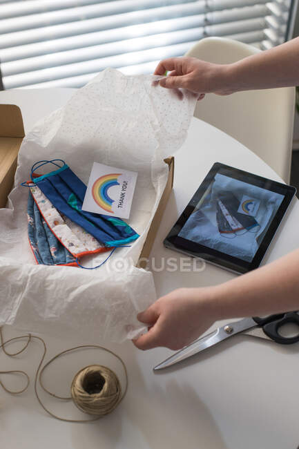 Cropped shot of woman packing handmade masks in box with thank you card — Stock Photo