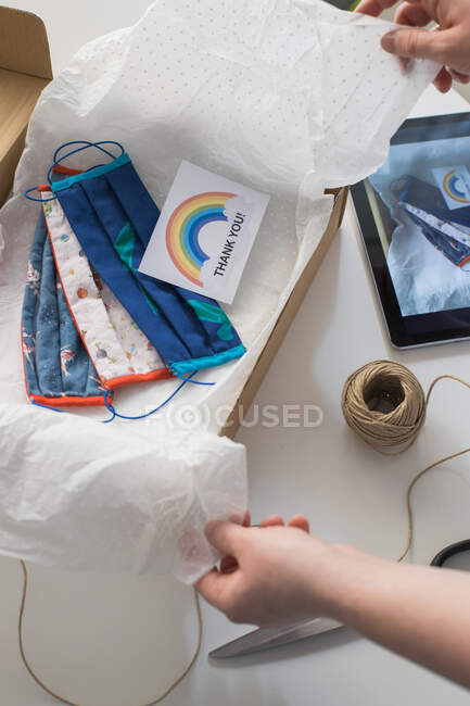 Cropped shot of woman packing handmade masks in box with thank you card — Stock Photo