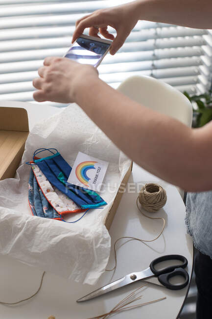 Cropped shot of woman taking photo of handmade masks with thank you card packed in box — Stock Photo