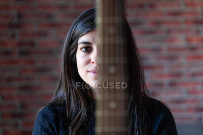 Portrait of a woman with an antique wooden guitar. The woman is in her house. Behind it is a brick wall — Stock Photo