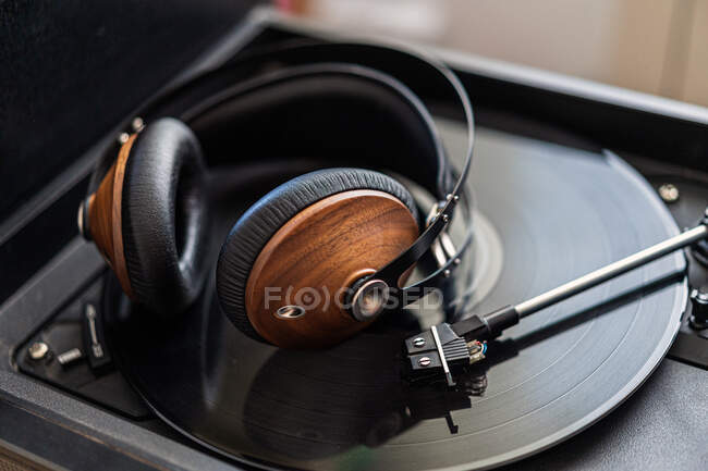 Vintage headphones made of wood are on a black vinyl in a record player — Stock Photo