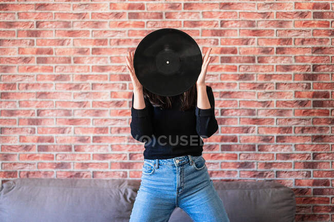 Mujer joven anónima sosteniendo un vinilo negro con sus manos - foto de stock