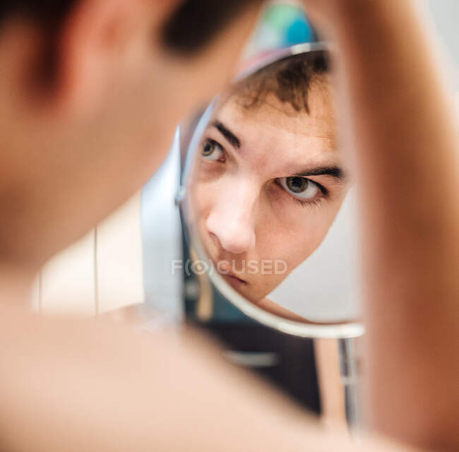 Sério masculino em pé no banheiro brilhante e olhando em espelho redondo de manhã — Fotografia de Stock