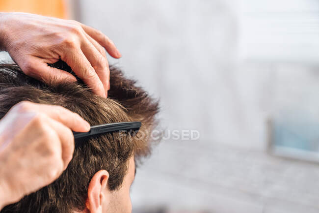 Crop man brossant les cheveux du jeune homme et faisant coiffure dans la salle de bain lumineuse — Photo de stock