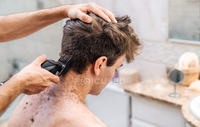 Male with hair trimmer cutting hair of guy in contemporary bathroom at home  — everyday, bright - Stock Photo | #384642376