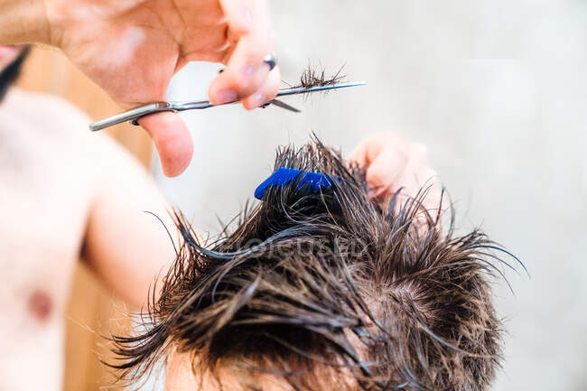 Maschio irriconoscibile che fa taglio di capelli al ragazzo con le forbici contro l'interno sfocato del bagno leggero a casa — Foto stock
