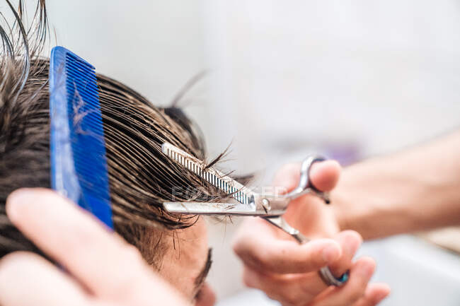Vista lateral de homem irreconhecível fazendo corte de cabelo para cara usando tesoura contra interior borrado de banheiro leve em casa — Fotografia de Stock