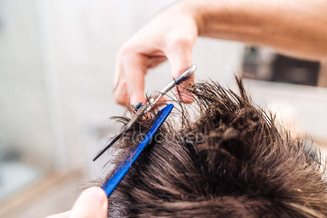 Vue arrière d'un homme méconnaissable faisant coupe de cheveux à l'aide de ciseaux contre l'intérieur flou de la salle de bain légère à la maison — Photo de stock