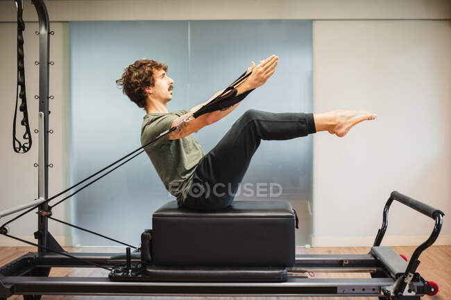 Side view of sportsman in activewear using pilates machine and stretching arms with resistance bands — Stock Photo
