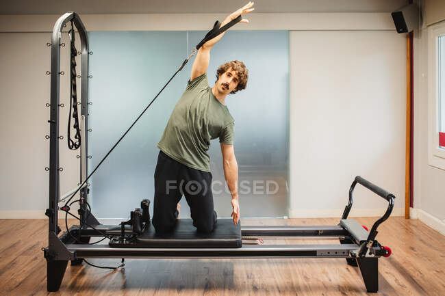 Sportsman en vêtements de sport utilisant une machine pilates et bras étirables avec des bandes de résistance — Photo de stock