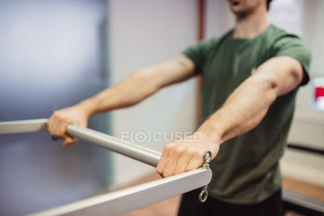Atleta masculino irreconocible en ropa deportiva haciendo ejercicios con un reformador de pilates durante el entrenamiento en el gimnasio - foto de stock