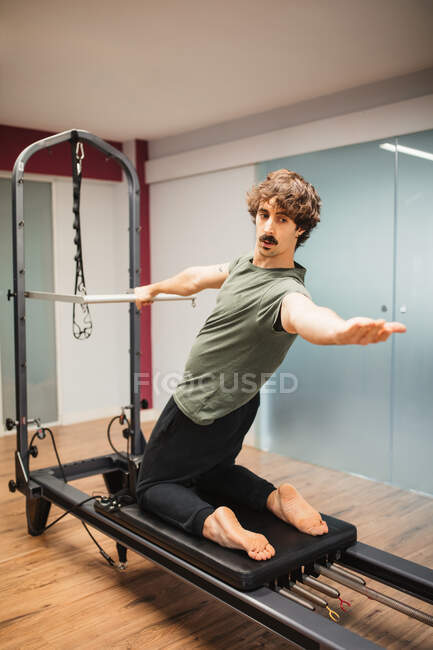 Спортсмен в спортивной форме делает упражнения с реформатором пилатеса во время тренировки в тренажерном зале — стоковое фото