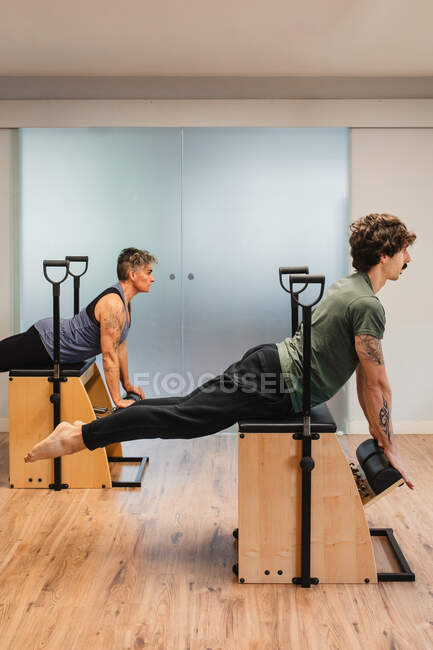 Vista laterale dello sportivo e dello sportivo in equilibrio sulla sedia pilates durante l'allenamento in palestra — Foto stock