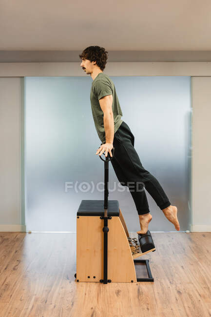 Side view of strong sportsman balancing on hands on pilates chair during workout in modern gym — Stock Photo