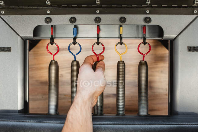 Crop man touching metal springs on hooks of modern pilates reformer placed in gym — Stock Photo