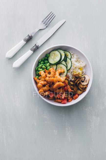 Top view of white poke bowl with rice and cucumber with beans and mushrooms topped with shrimps — Stock Photo
