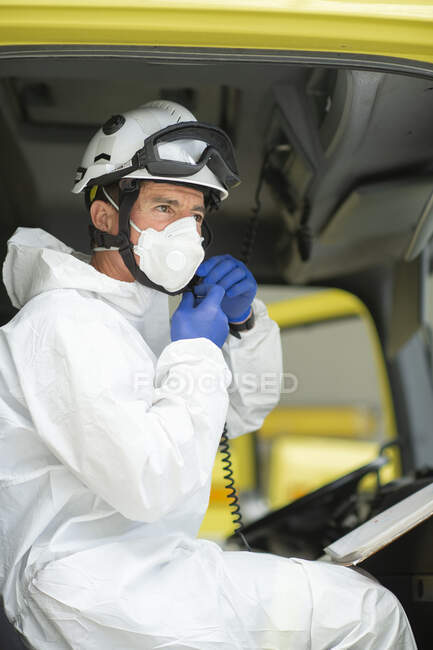 Side view serious firefighter wearing respirator and helmet sitting in fire car — Stock Photo
