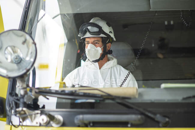 Bombeiro sério usando respirador e capacete sentado no carro de bombeiros — Fotografia de Stock