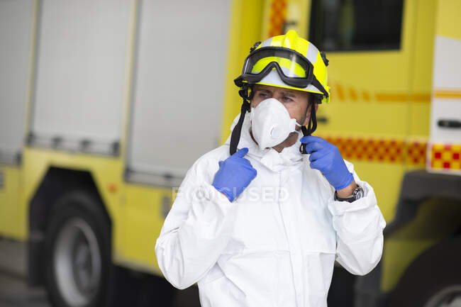 Serious fireman in protective costume and wearing respirator on fire station during coronavirus pandemic — Stock Photo