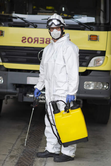 Male firefighter in protective uniform and hardhat standing near fire engine and preparing for disinfection while looking at camera — Stock Photo