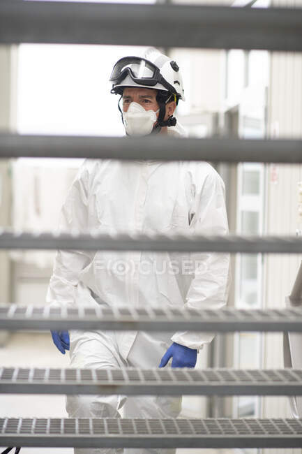 Male firefighter in protective helmet and respirator walking upstairs at fire station and looking away — Stock Photo