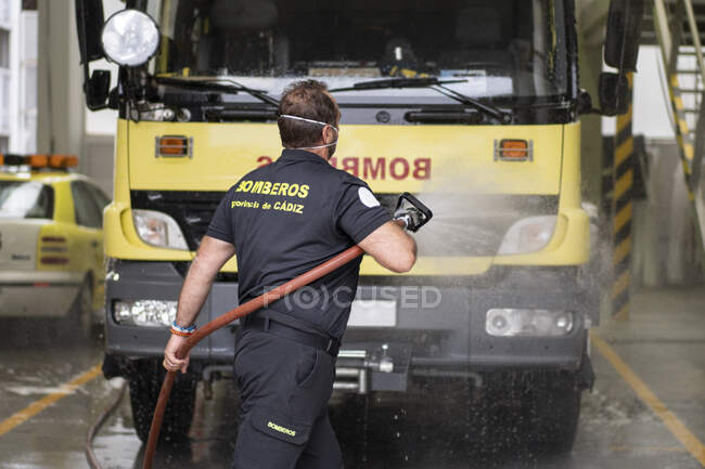Back view of firefighter washing car with fire hose at station — Stock Photo
