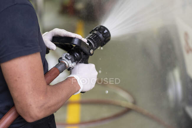 Side view of unrecognizable firefighter in latex gloves washing car with fire hose at station — Stock Photo