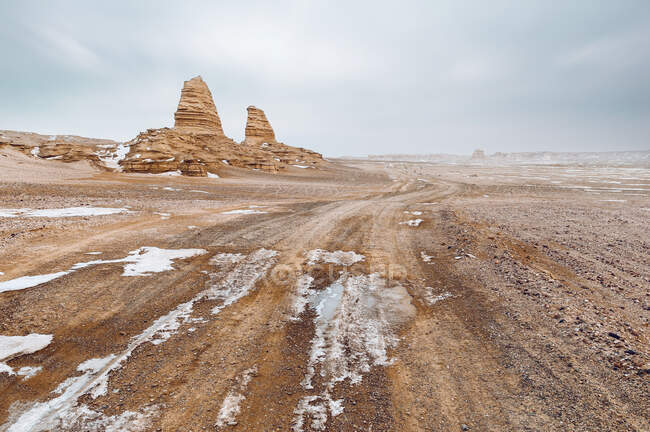 Formazione rocciosa nella scena desertica innevata sotto il cielo nuvoloso — Foto stock