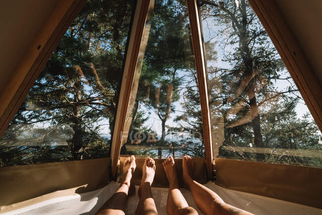 Piedi di fidanzato e fidanzata sdraiati insieme in amaca in camp house e ammirando la vista del legno attraverso la finestra — Foto stock