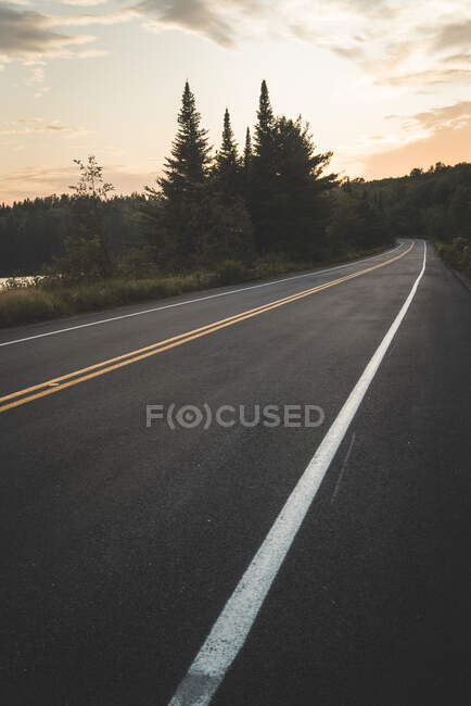 Strada asfaltata in prossimità di lago tranquillo e foresta verde contro cielo nuvoloso tramonto nel Parco Nazionale La Mauricie in Quebec, Canada — Foto stock