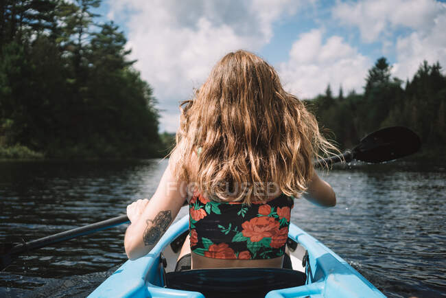 Back view of anonymous female traveler in life vest sitting in boat during river exploration against cloudy sky in La Mauricie National Park in Quebec, Canada — Stock Photo