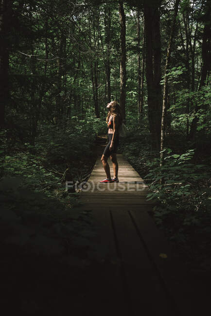 Vista laterale della donna con zaino in piedi sul sentiero del legname e godersi il tempo nella foresta verde del Parco Nazionale La Mauricie in Quebec, Canada — Foto stock