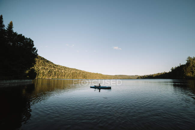 Silhouette of anonymous male traveler sitting on kayak and rowing during trip on calm river on cloudless day in La Mauricie National Park in Quebec, Canada — Stock Photo