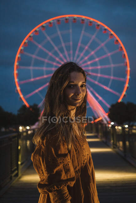 Junge Touristin steht auf beleuchtetem Pier und blickt in Kamera mit leuchtendem Riesenrad im Hintergrund in Montreal — Stockfoto