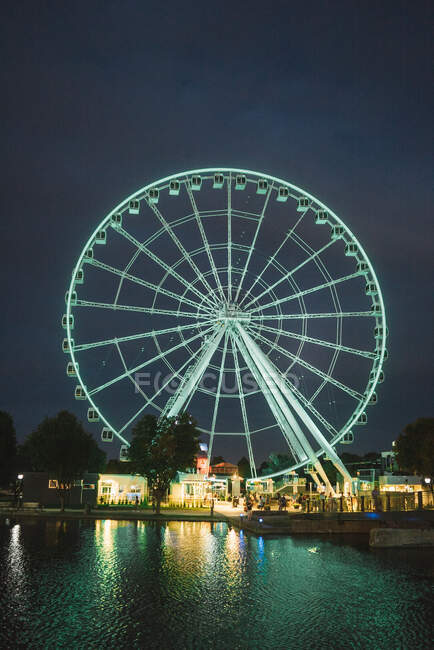 Blue glowing Ferris wheel in amusement park on pier of Montreal city reflecting in river water at night — Stock Photo