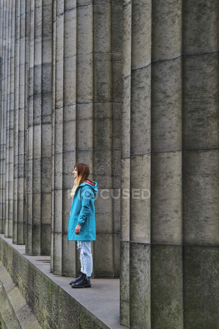 Side view of woman in colorful jacket standing on ancient memorial monument with symmetrical ribbed concrete columns — Stock Photo