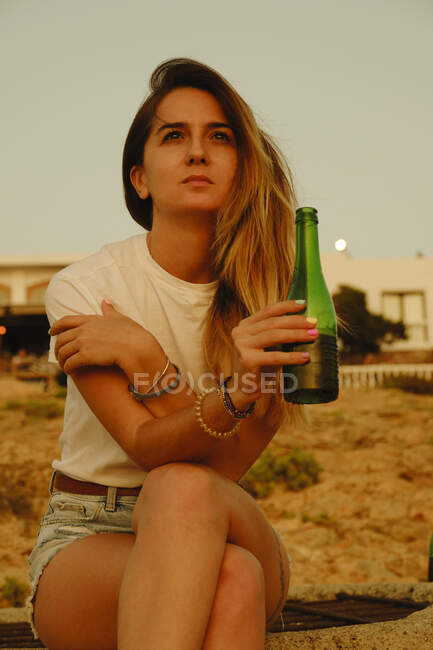 Молода леді з пляшкою пива під час заходу сонця на березі моря — стокове фото