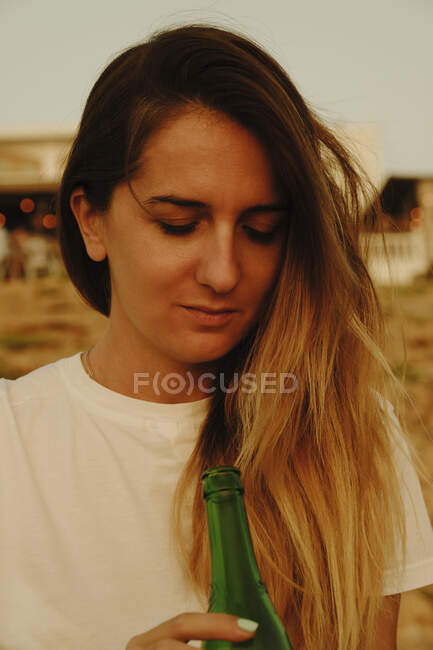Giovane signora con bottiglia di birra durante il tramonto in riva al mare — Foto stock