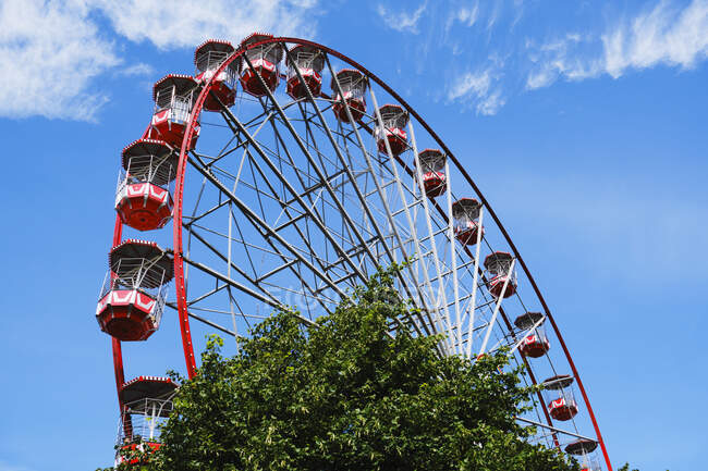 De baixo da roda gigante com cabines vermelhas localizadas no parque de diversões com árvores e torre no dia ensolarado com céu azul — Fotografia de Stock