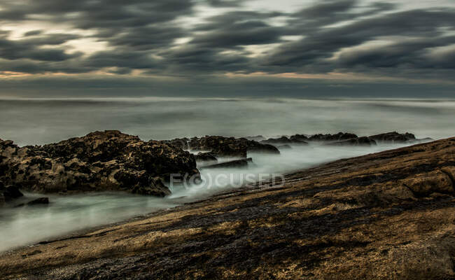 Cenário pitoresco de terreno rochoso enquanto ondas dramáticas batendo pedras na Cantábria em dia nublado cinza — Fotografia de Stock