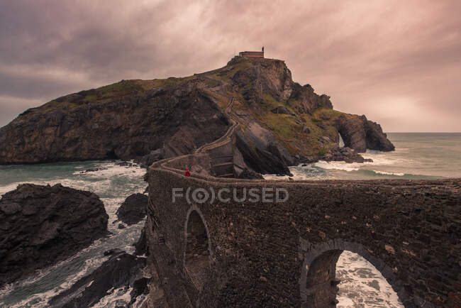 Malerische Landschaft der Insel Gaztelugatxe mit langer Steinbrücke, die bei windigem Wetter durch die Küste führt — Stockfoto