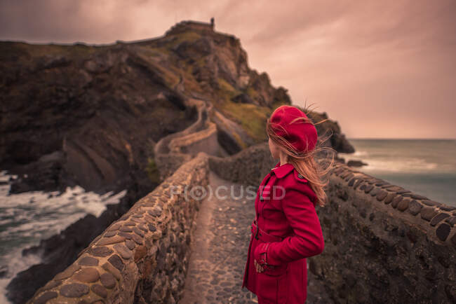 Vista posteriore di turista donna irriconoscibile in abiti caldi a piedi verso ponte cappella durante il viaggio sull'isola di San Juan de Gaztelugatxe in Spagna — Foto stock