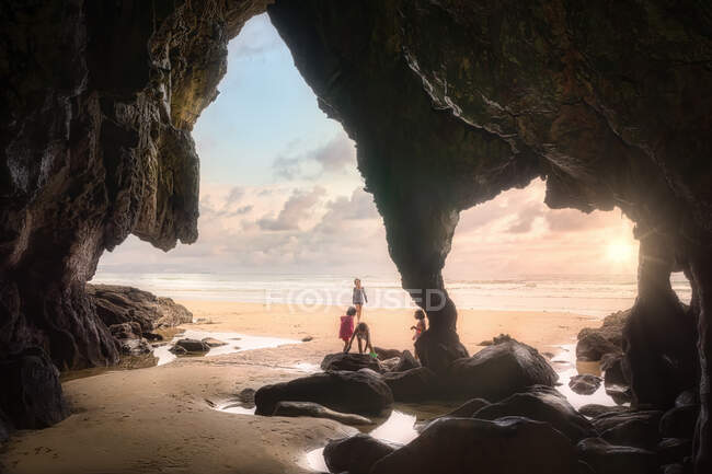 Scenic view of distance children having fun and playing on sandy seashore next to amazing cave on hot summer sunset evening — Stock Photo