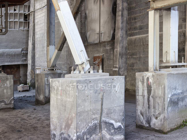 Детали массивных выветриваемых металлических конструкций, размещенных на бетонном грунте, расположенном в заброшенном цехе обветшалого промышленного здания — стоковое фото
