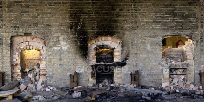 Amplia vista angular de la pared de piedra envejecida con hornos destruidos y basura dentro de una fábrica industrial abandonada - foto de stock