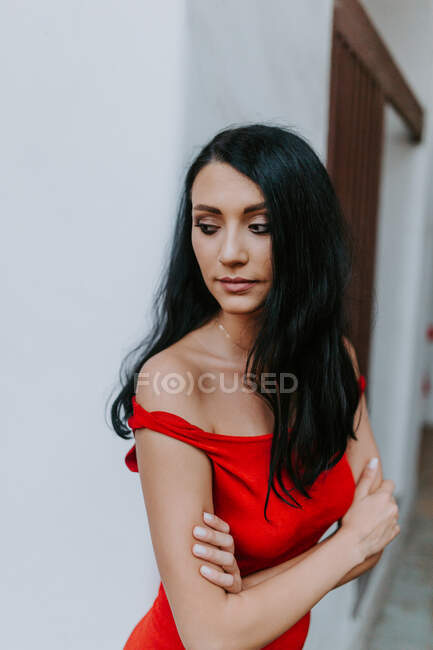 Vista laterale di attraente giovane signora in elegante abito rosso braccia incrociate — Foto stock