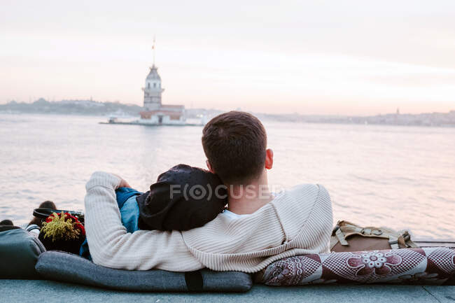 Задний вид анонимной любящей пары, сидящей на подушках на набережной и наслаждающейся прекрасным закатом во время романтического свидания в Стамбуле — стоковое фото